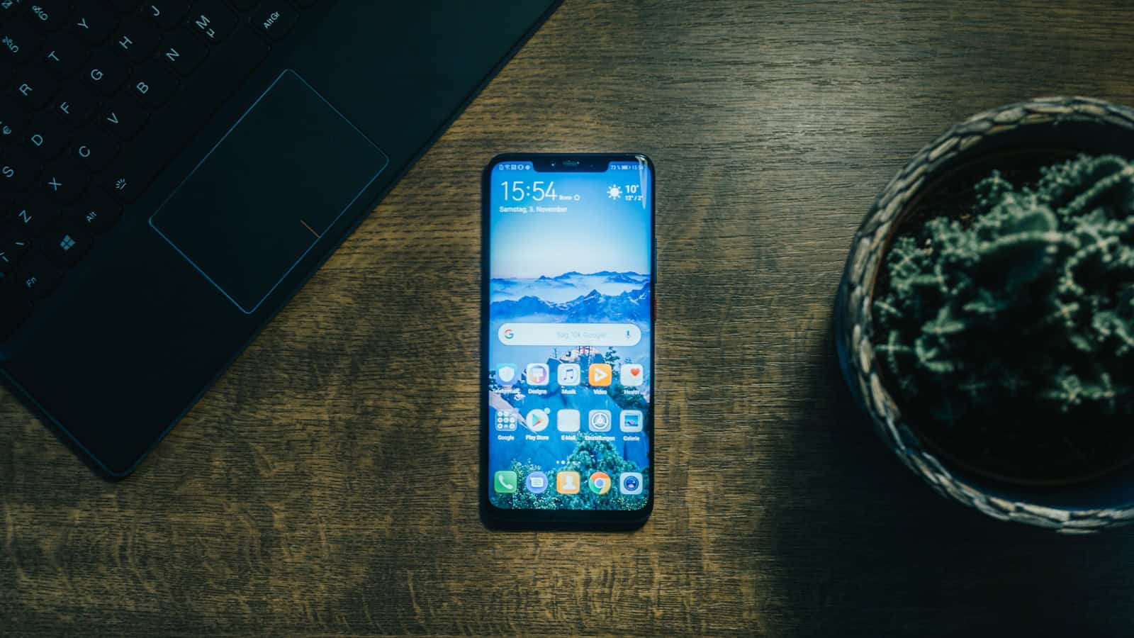 An Android phone lying on a desk beside an open laptop keyboard.