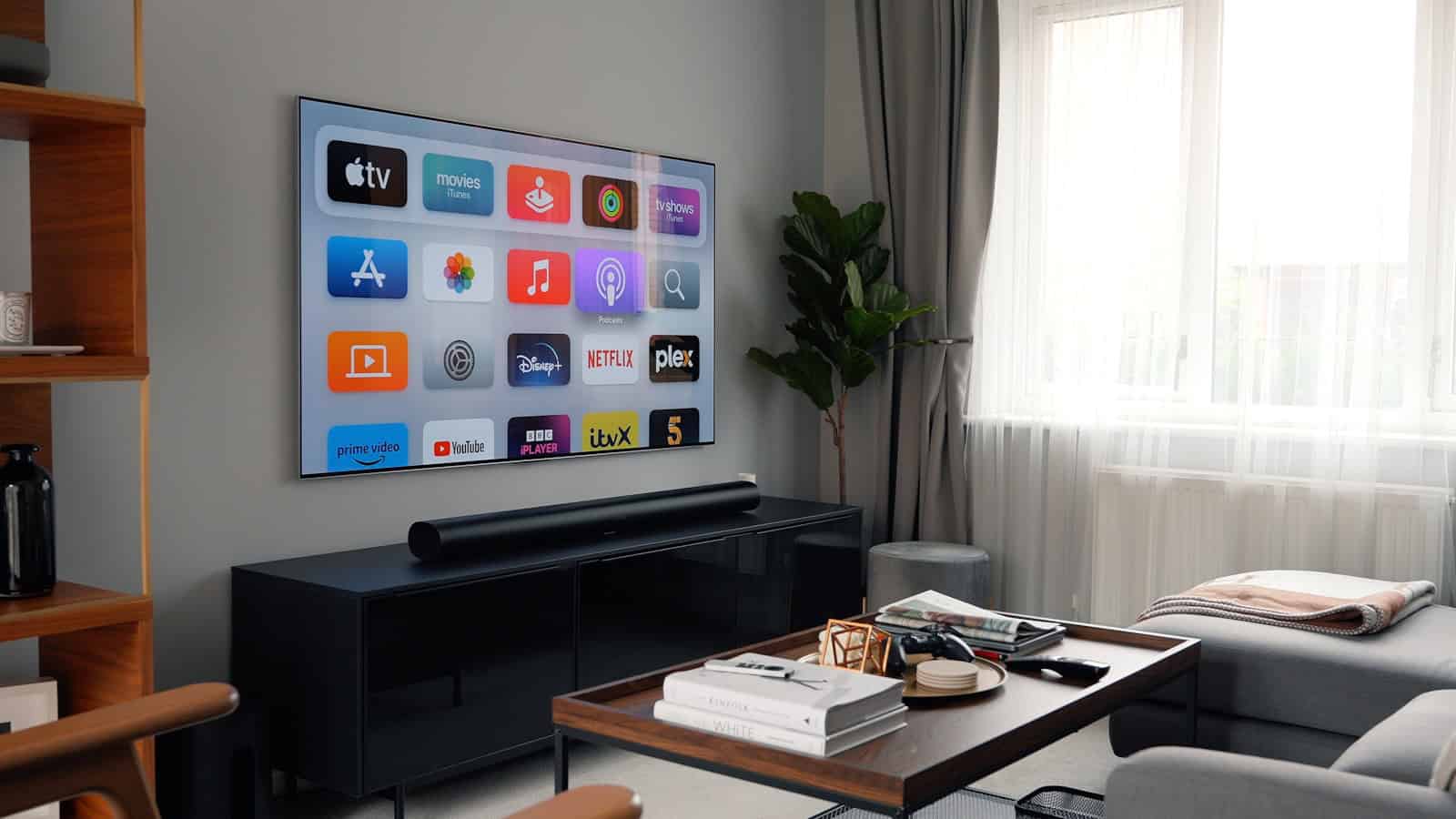 A wall-mounted TV showing the Apple TV home screen, with a soundbar on the media unit directly below it in a living room