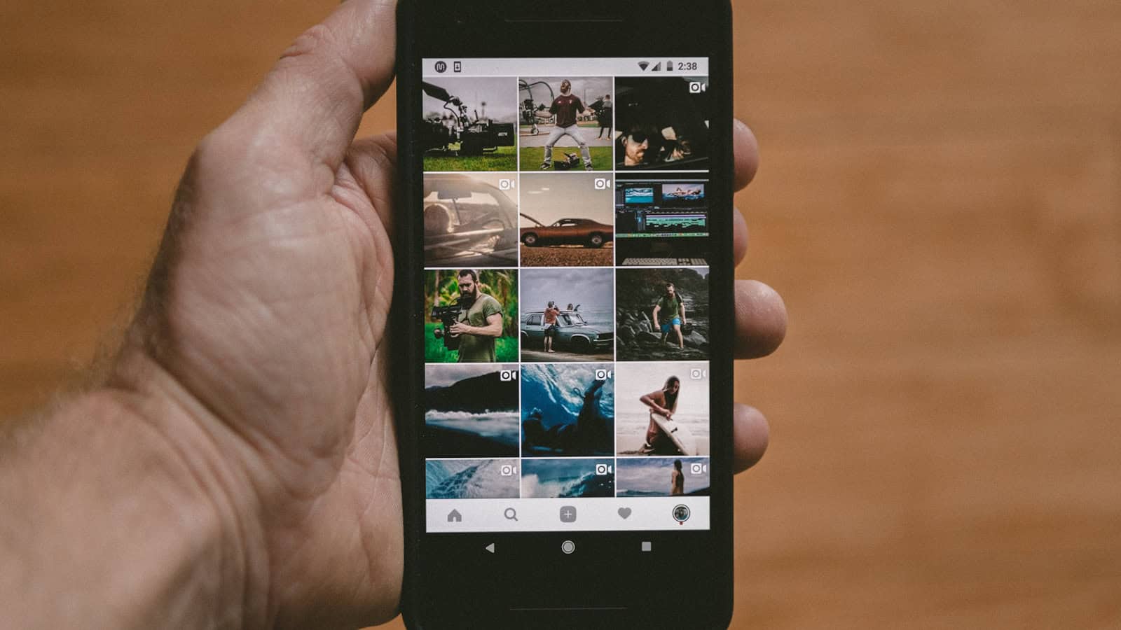 A hand holding an Android phone displaying a grid of photo thumbnails in a gallery app.
