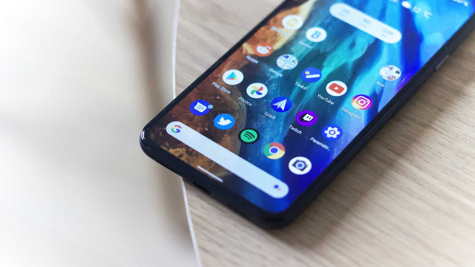 An Android phone lying on a light surface showing a home screen with app icons and a search bar.