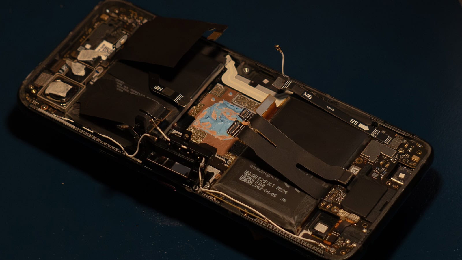 An opened phone shell on a dark surface with its internal battery and ribbon cables exposed.