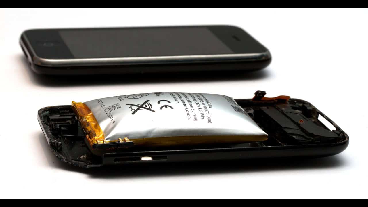 A swollen lithium-ion phone battery bulging out of its case, next to an intact phone for scale.