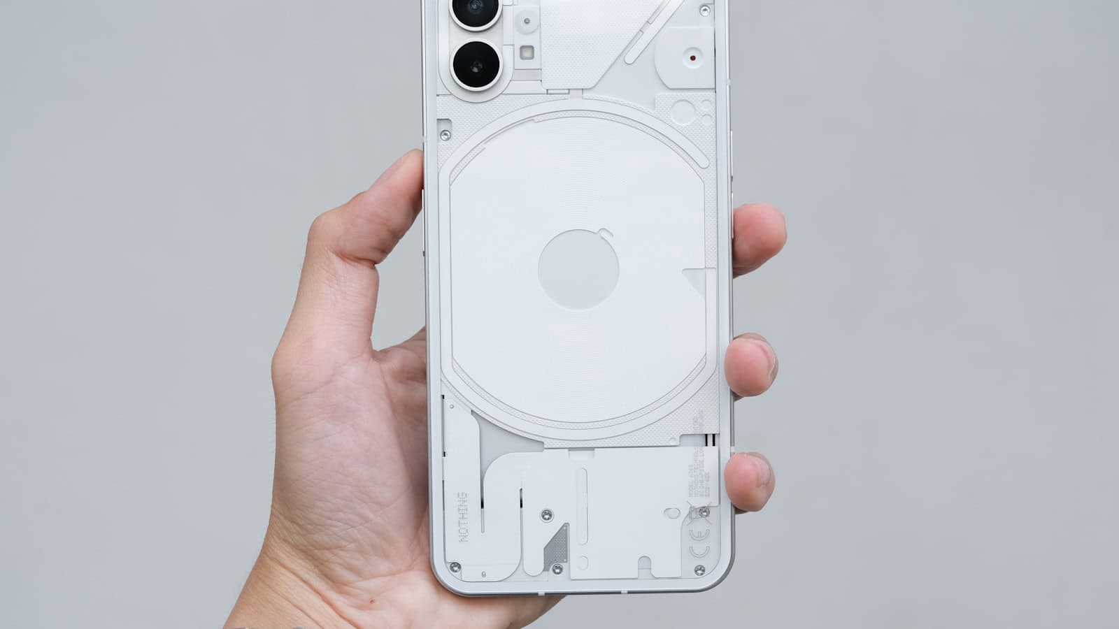 A hand holding a white Nothing Phone with its transparent back and glyph lighting facing the camera.