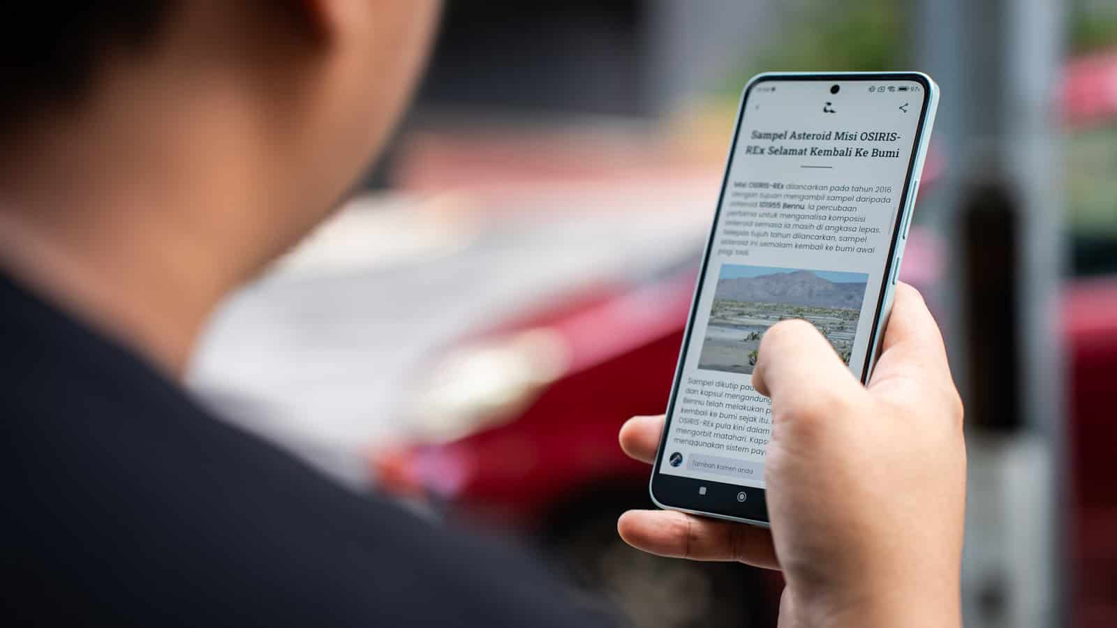 A person outdoors holding an Android phone that is displaying a news article in a browser.