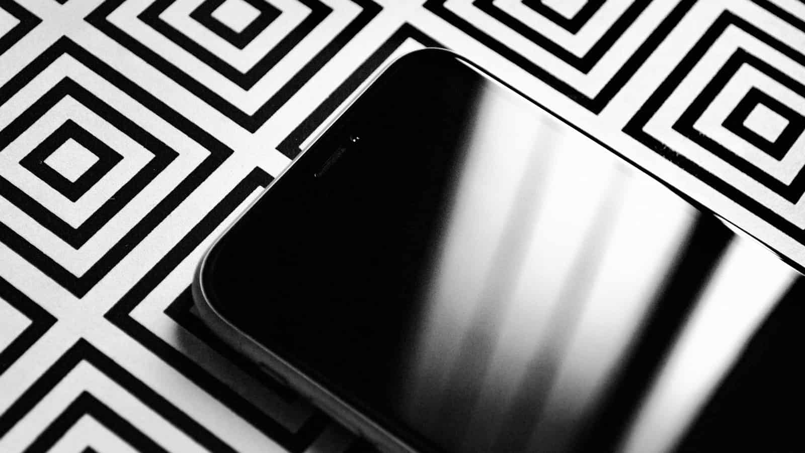 A smartphone lying face up on a patterned surface with a dark, reflective screen.