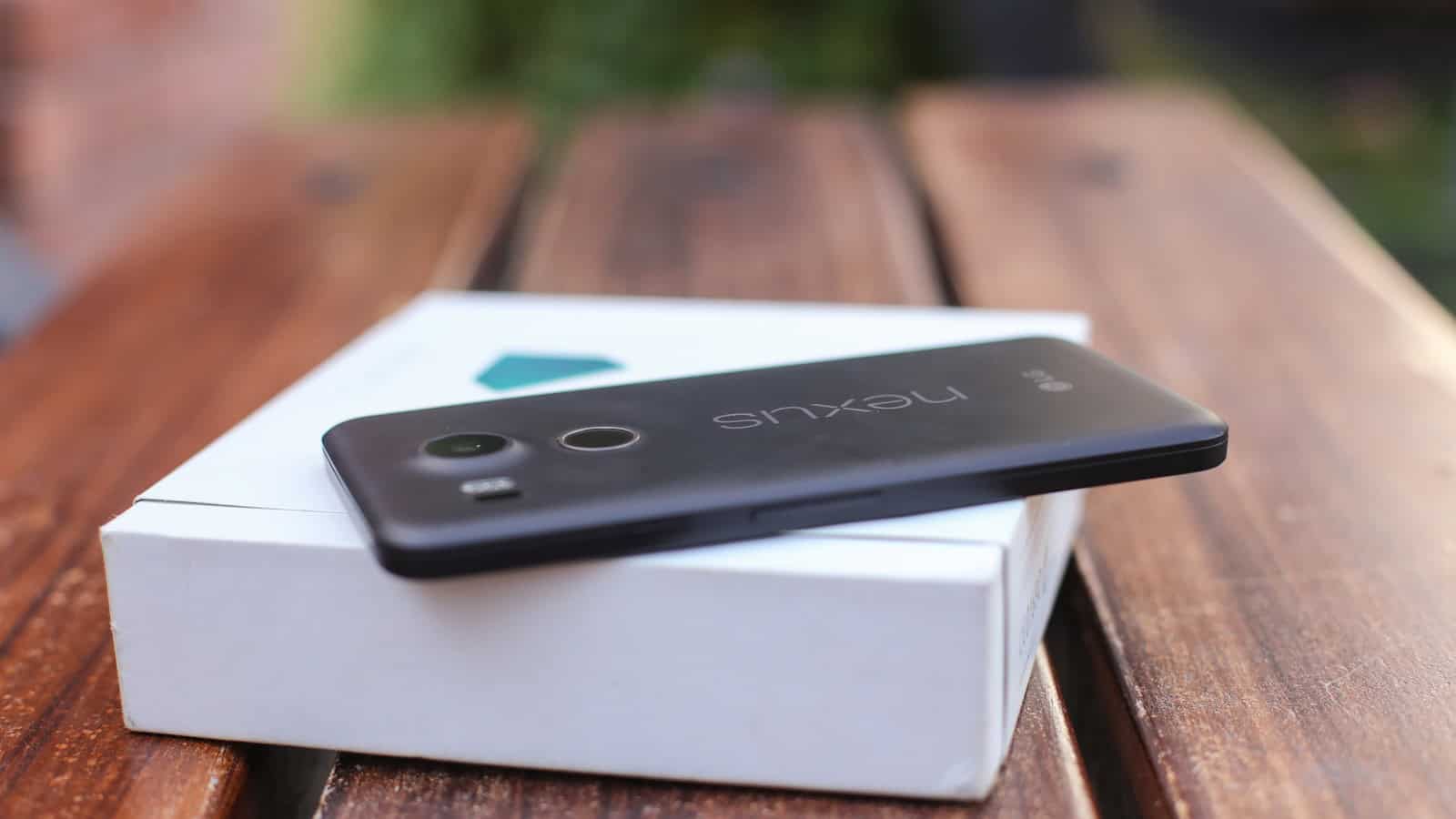 An older Android phone resting on top of its white retail box on a wooden bench.