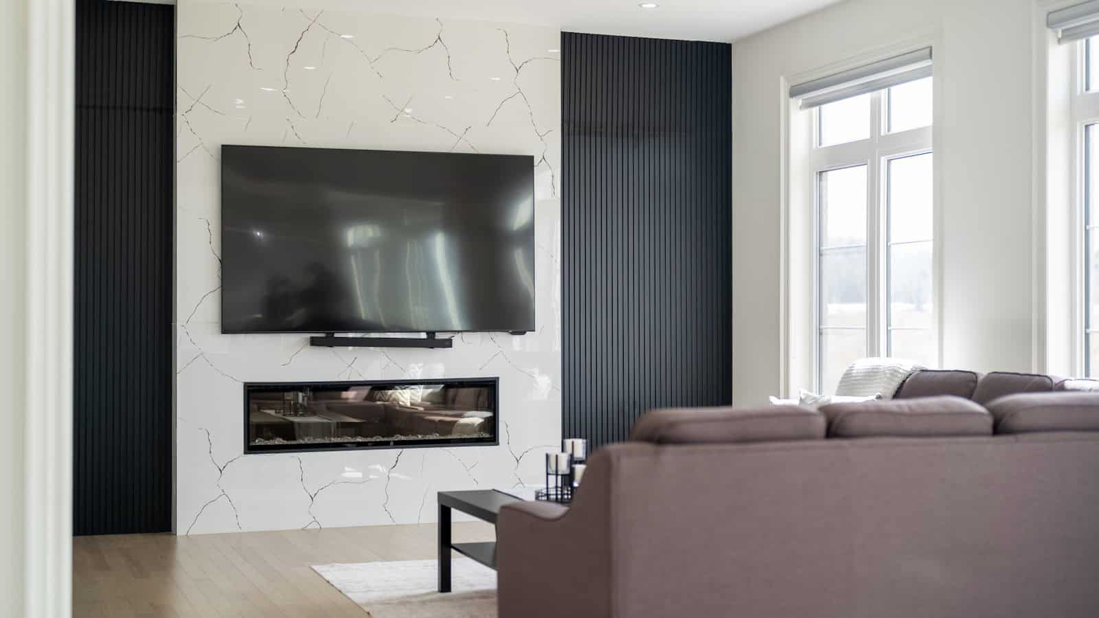 A large flat-screen TV mounted on a white marble wall above a fireplace in a living room.