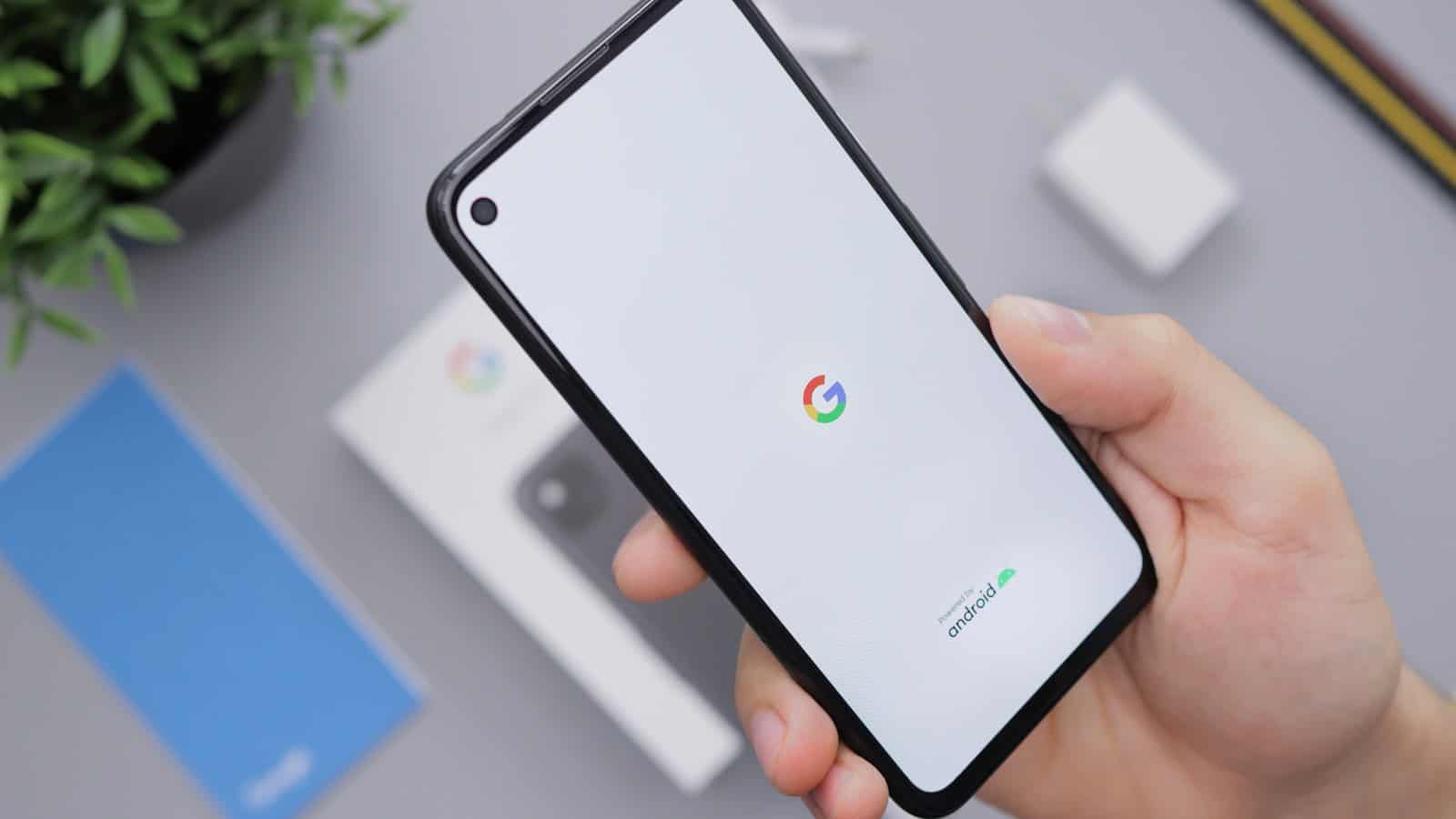 A hand holding an Android phone showing the Google search page on its screen.