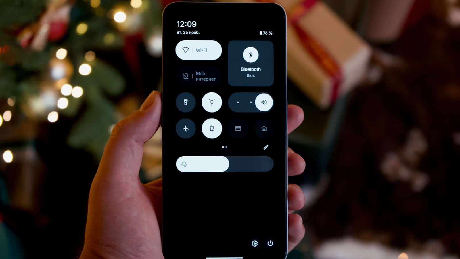 A hand holding a phone with the shade pulled down over its quick settings toggles.