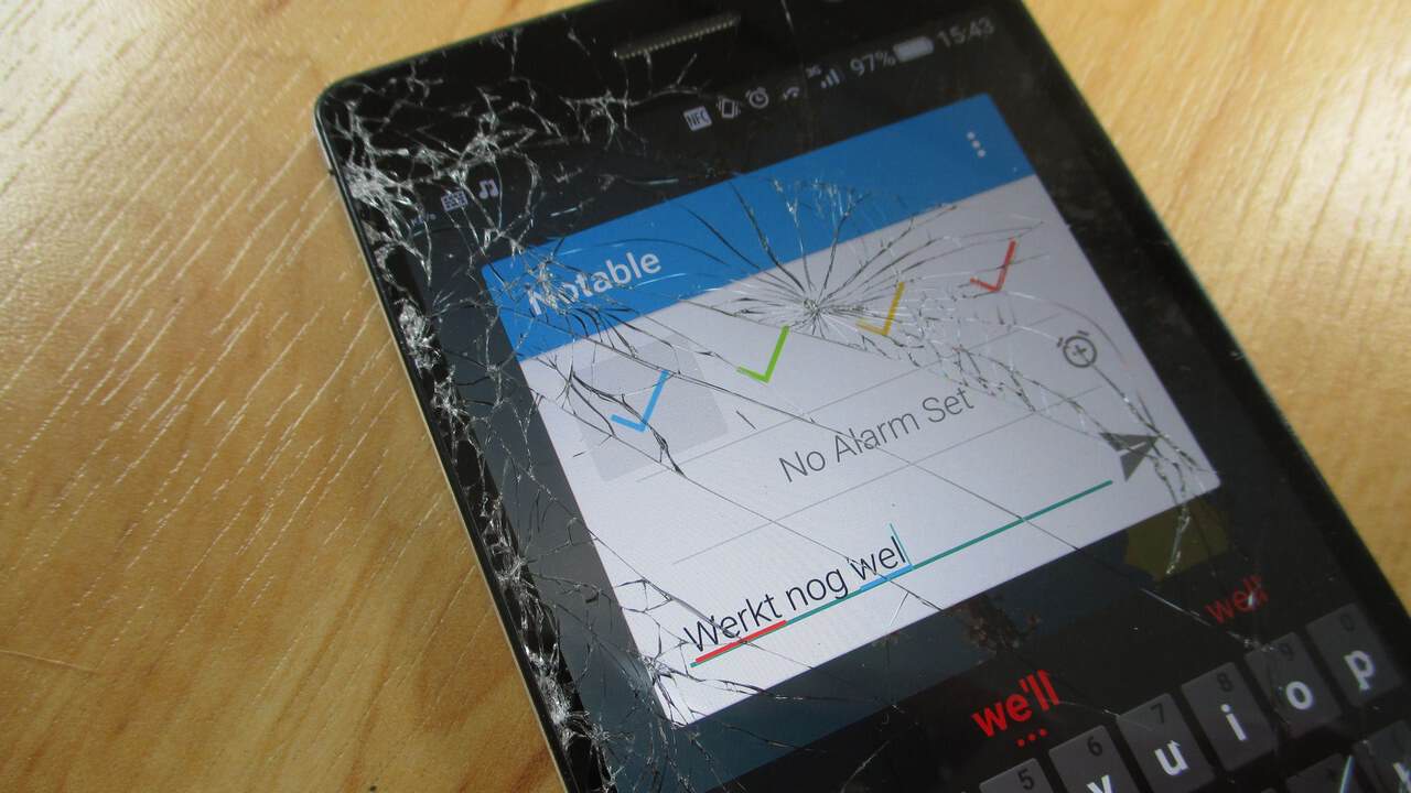 A smartphone with a badly shattered front glass screen, still switched on and showing an app.