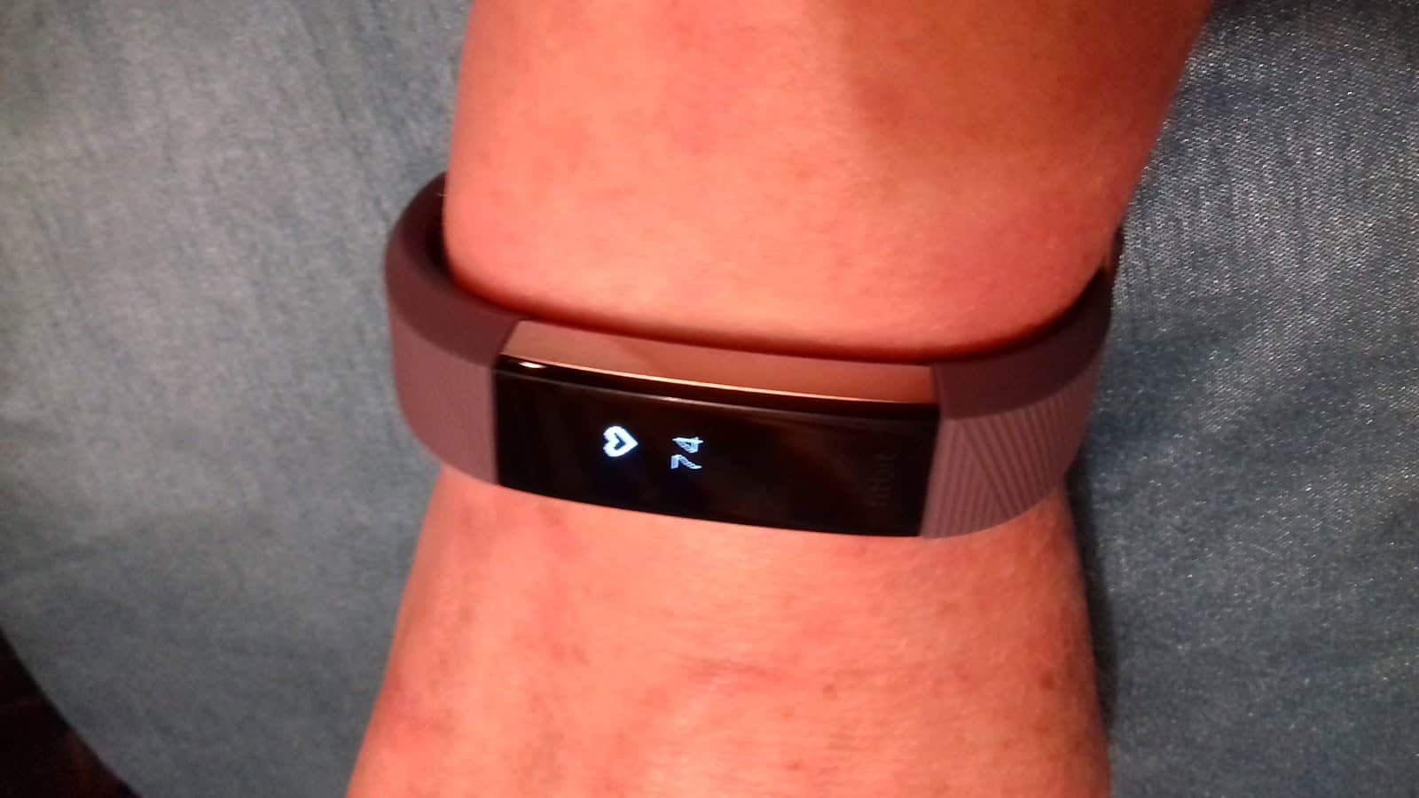 A Fitbit Alta HR fitness tracker worn on a wrist, showing a heart rate reading on its screen