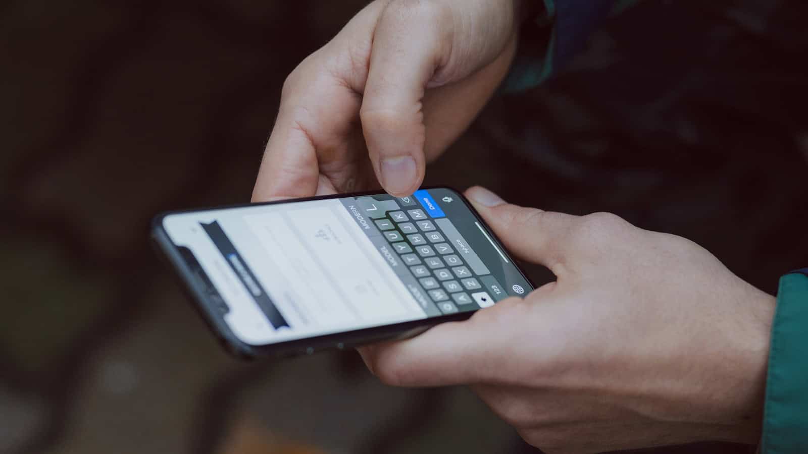Two hands holding a phone in landscape and typing on the on-screen keyboard.