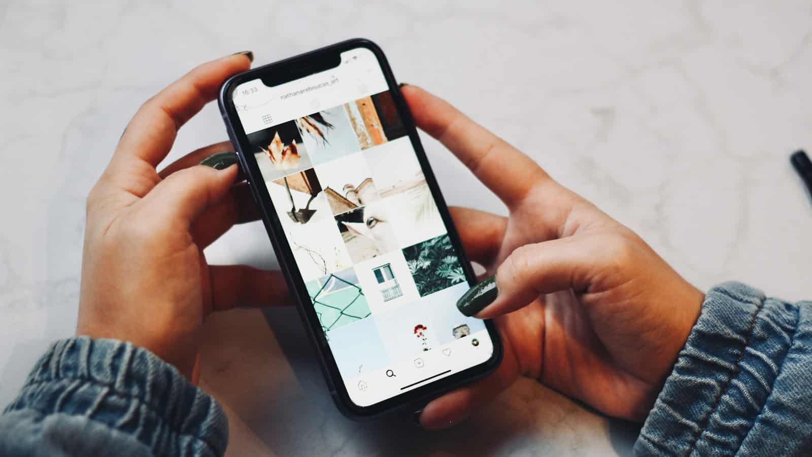 Two hands holding a phone showing a grid of photos in an app.