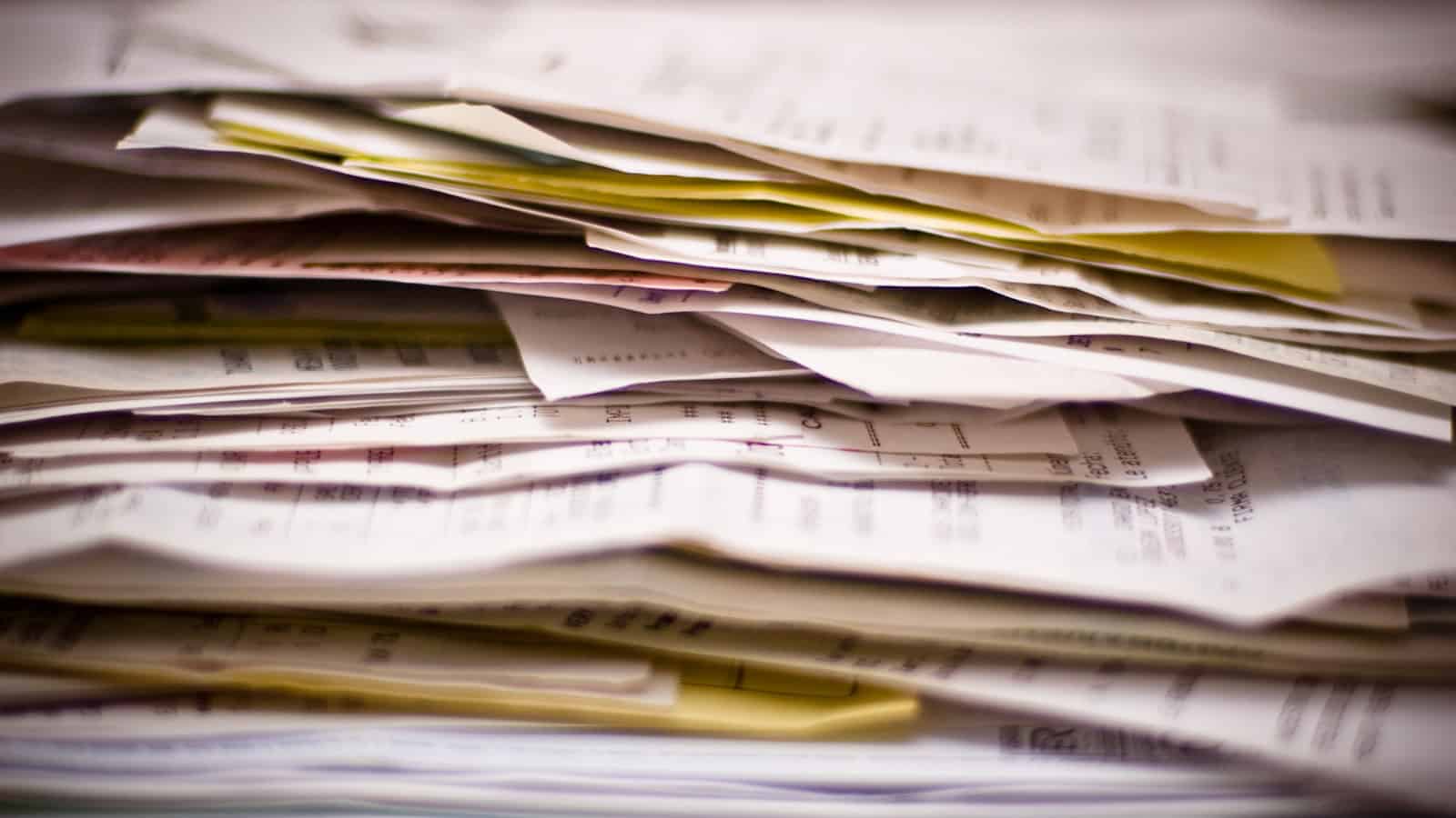 A thick, untidy stack of papers and envelopes piled on a desk.