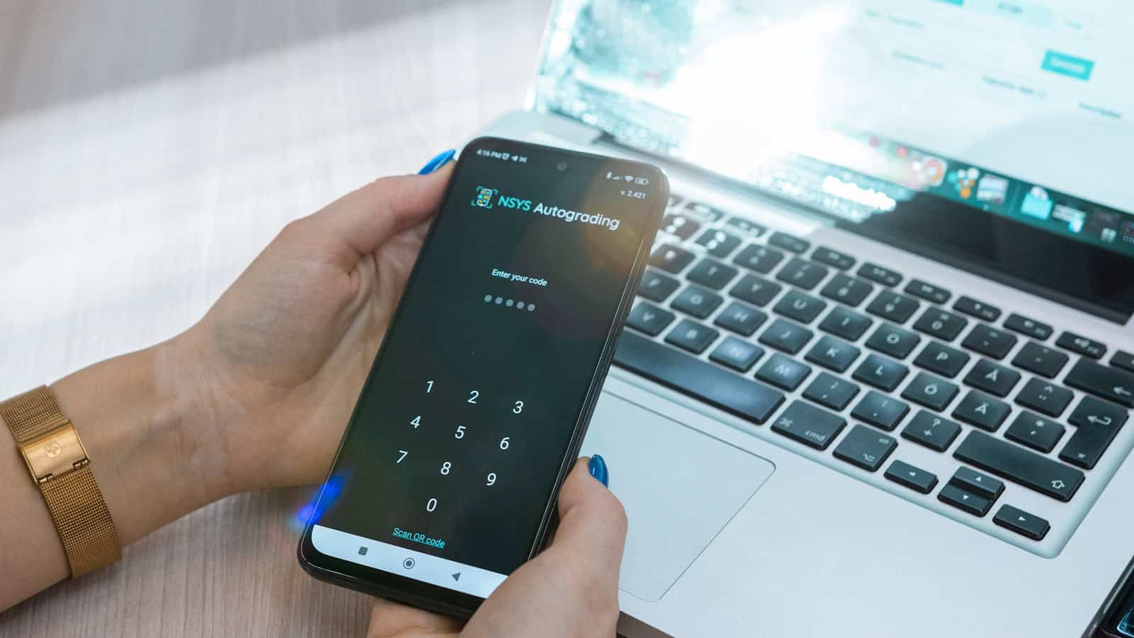 A person entering a passcode on a phone while sitting in front of an open laptop.