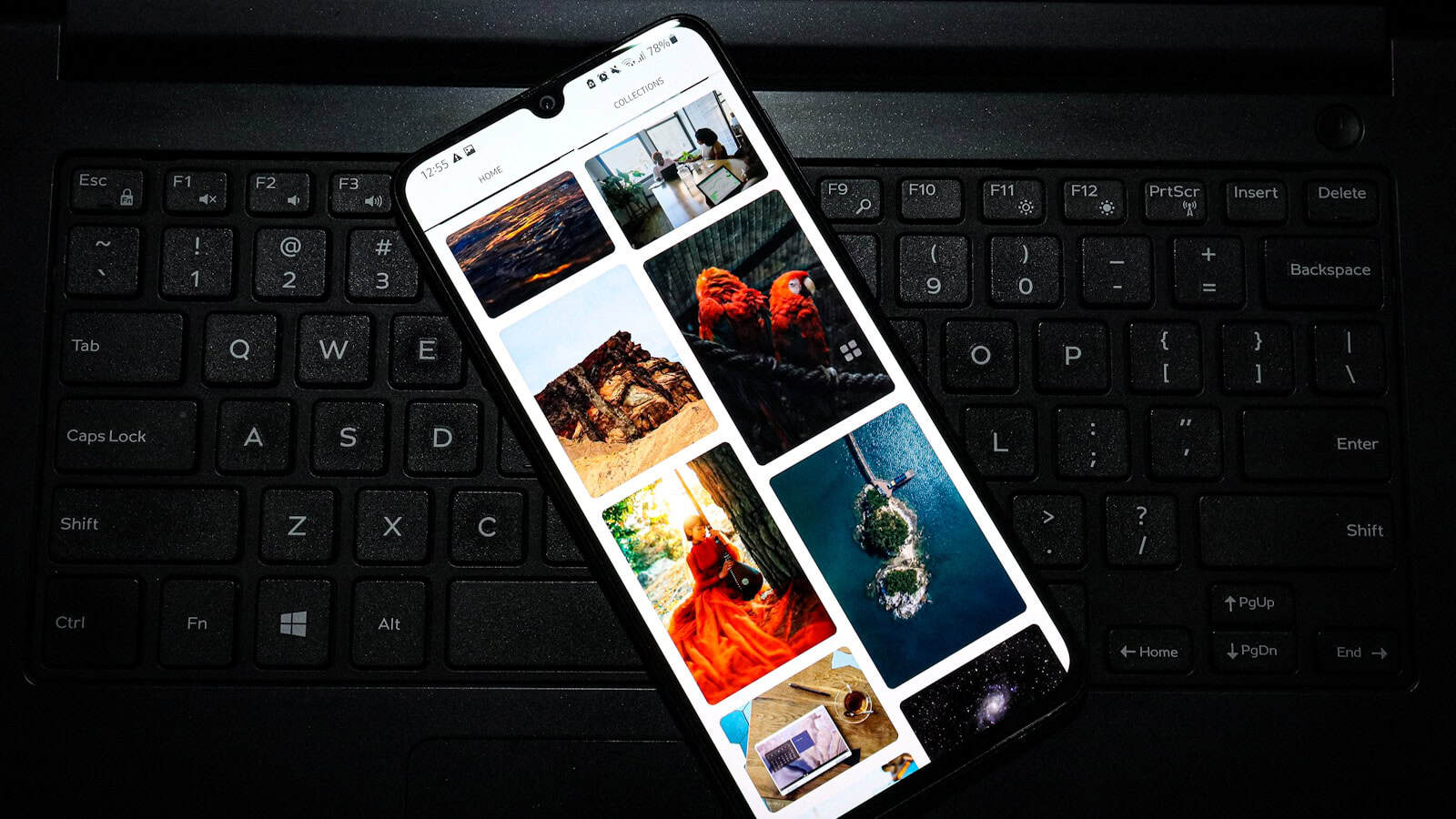 An Android phone resting on a laptop keyboard showing a grid of photo thumbnails.