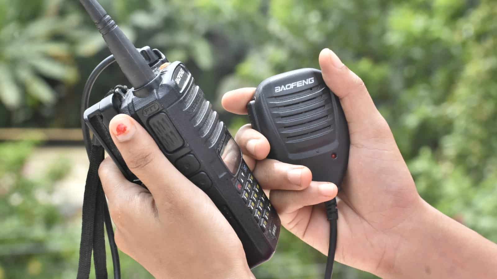 A person operating a Baofeng handheld ham radio with a speaker-microphone outdoors