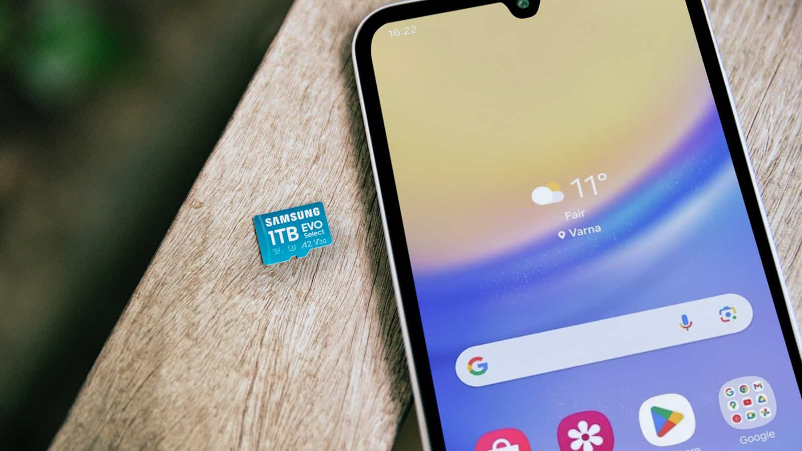A Samsung phone lying on a wooden table with a microSD card resting beside it.