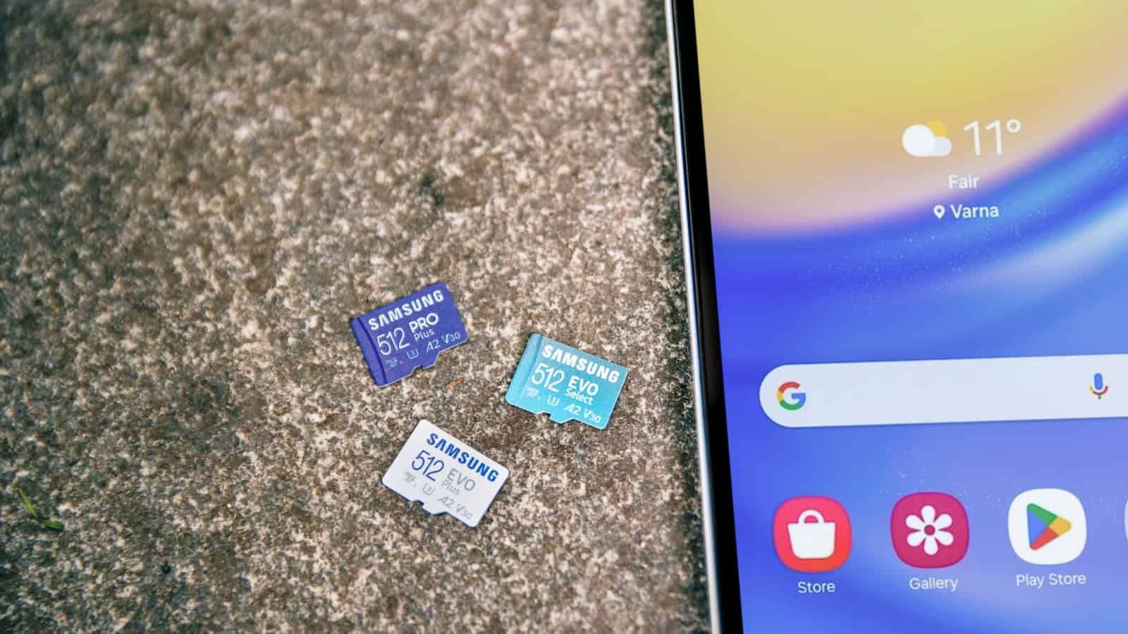 Three microSD cards lying on concrete beside an Android phone showing its home screen.