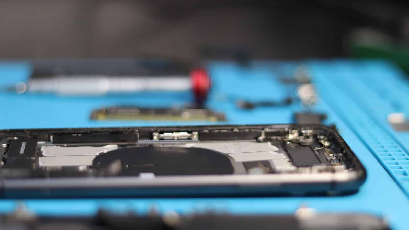 An opened phone chassis on a repair mat with its internal battery exposed.