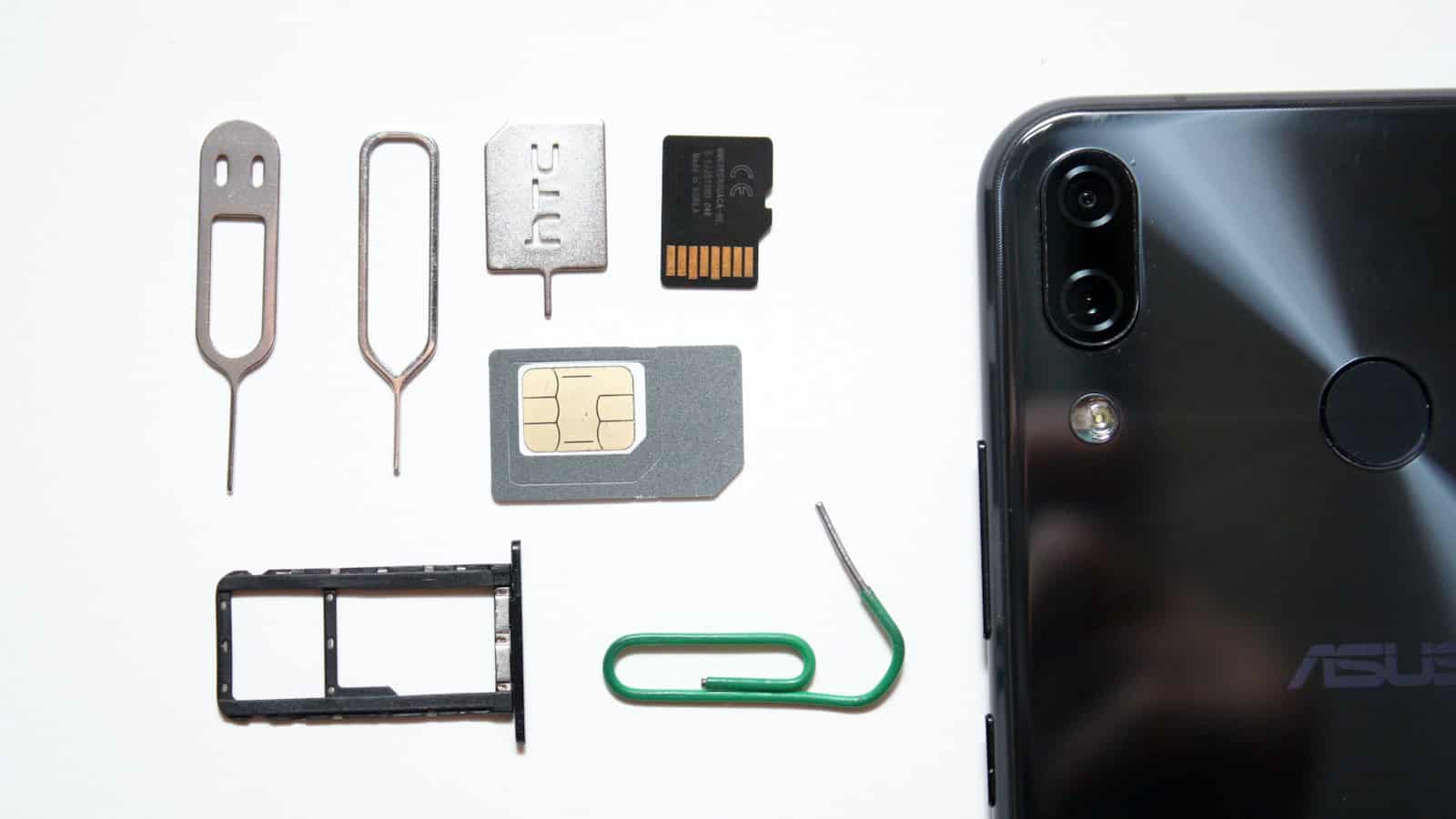 A SIM tray, ejector pin, SIM card and microSD card laid out beside the back of an Android phone.