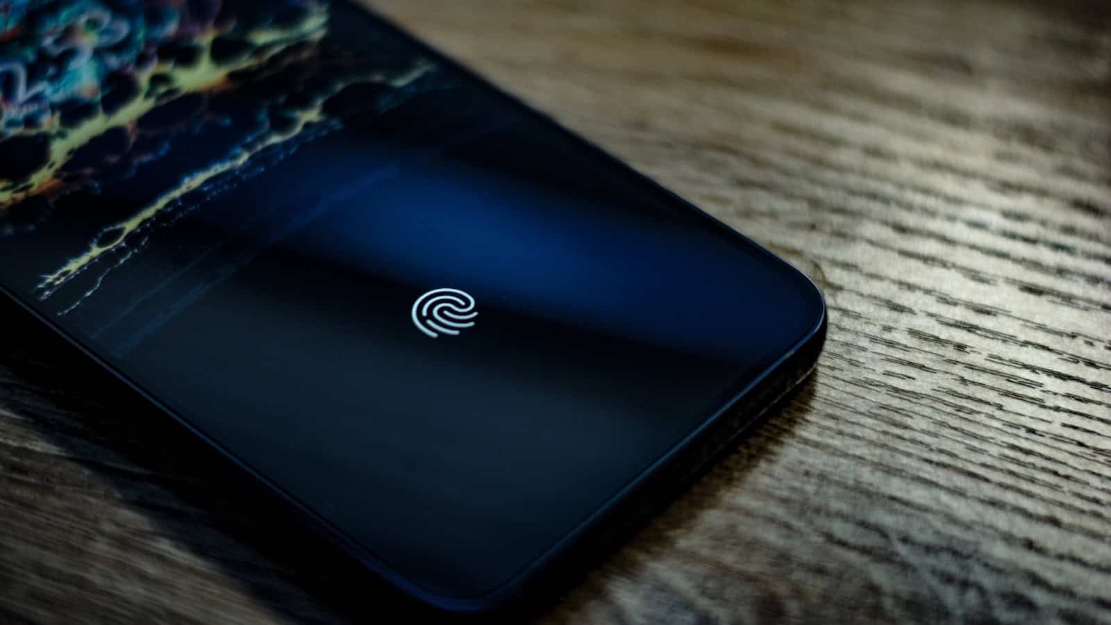A fingerprint icon glowing on an Android phone lock screen resting on a wooden table.