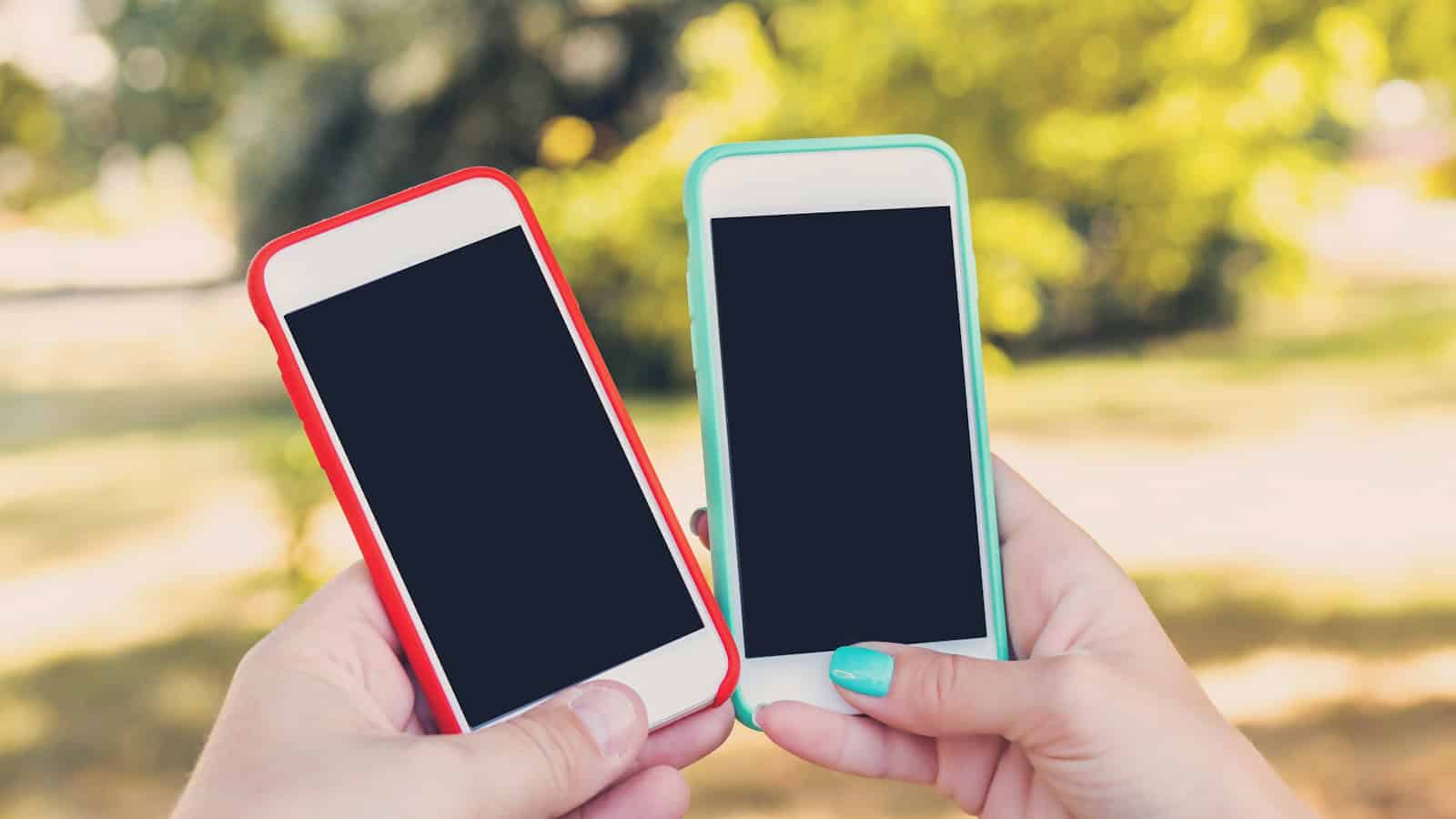 Two hands holding two phones back to back, both screens dark, outdoors.