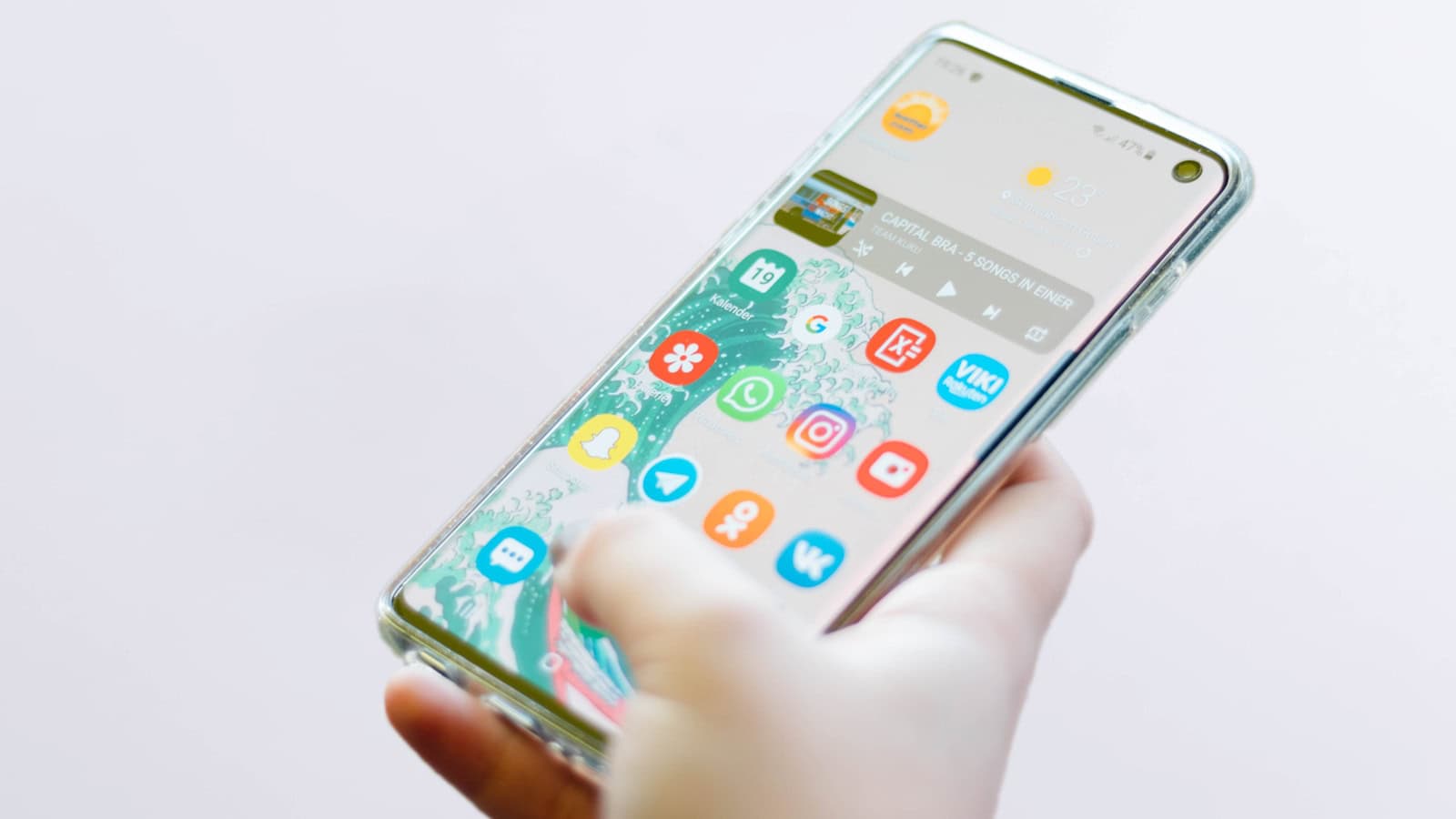 A hand scrolling the app-covered home screen of a Samsung Galaxy phone.