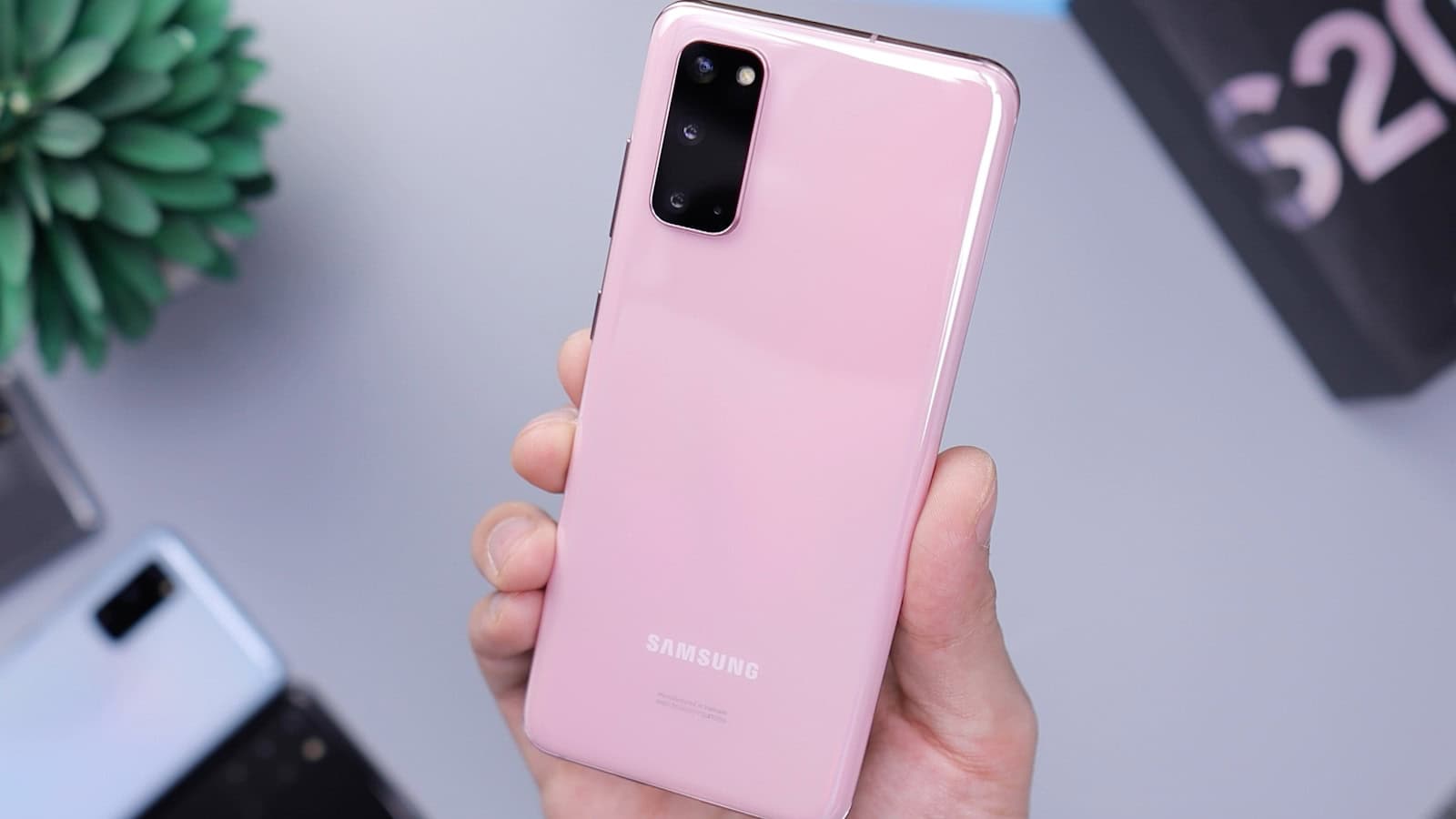 A hand holding a pink Samsung Galaxy phone from behind, the Samsung logo visible.