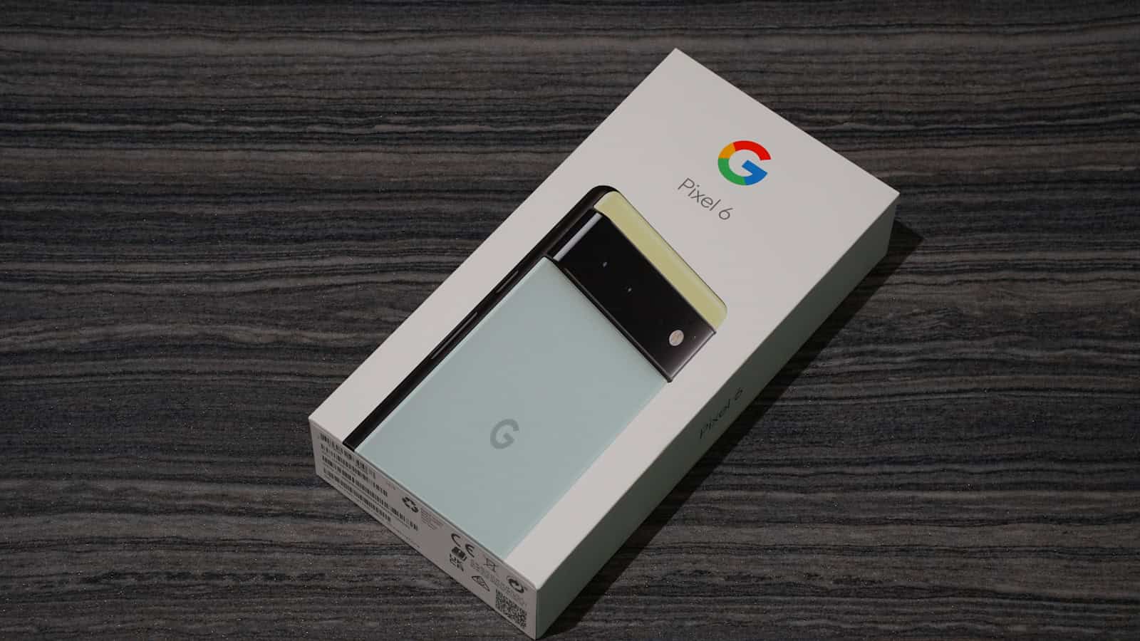 A Google Pixel phone resting on its opened retail box on a dark wooden surface.