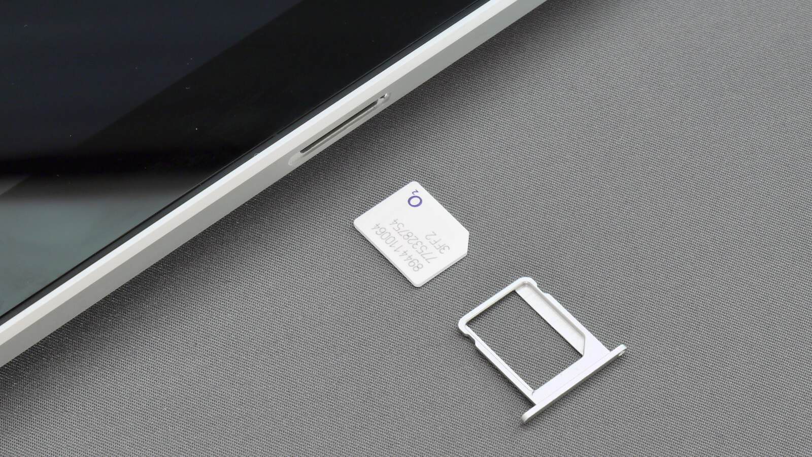 A phone lying face down with its SIM tray ejected and resting on the table beside it.