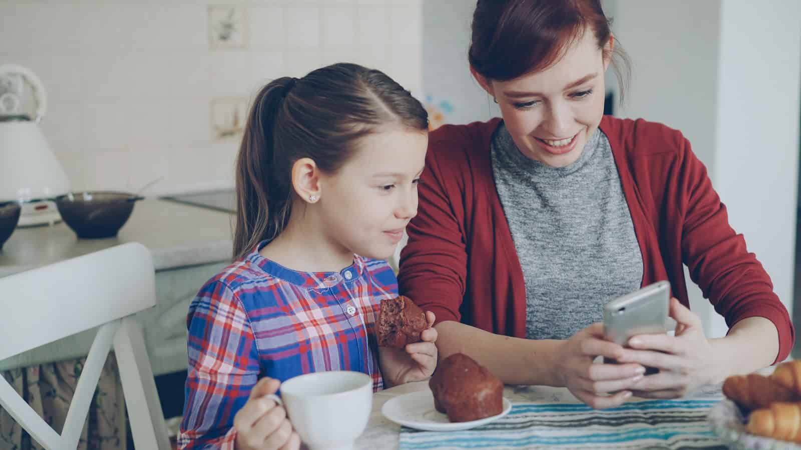 A woman and a girl at a breakfast table, each holding a phone.