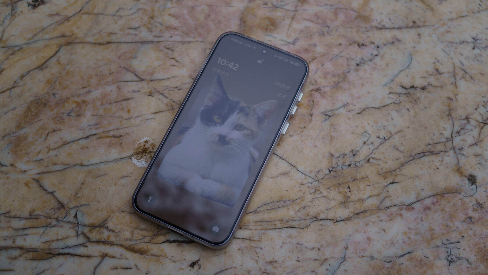 An older Android phone resting screen-up on a marble surface with its lock screen showing.