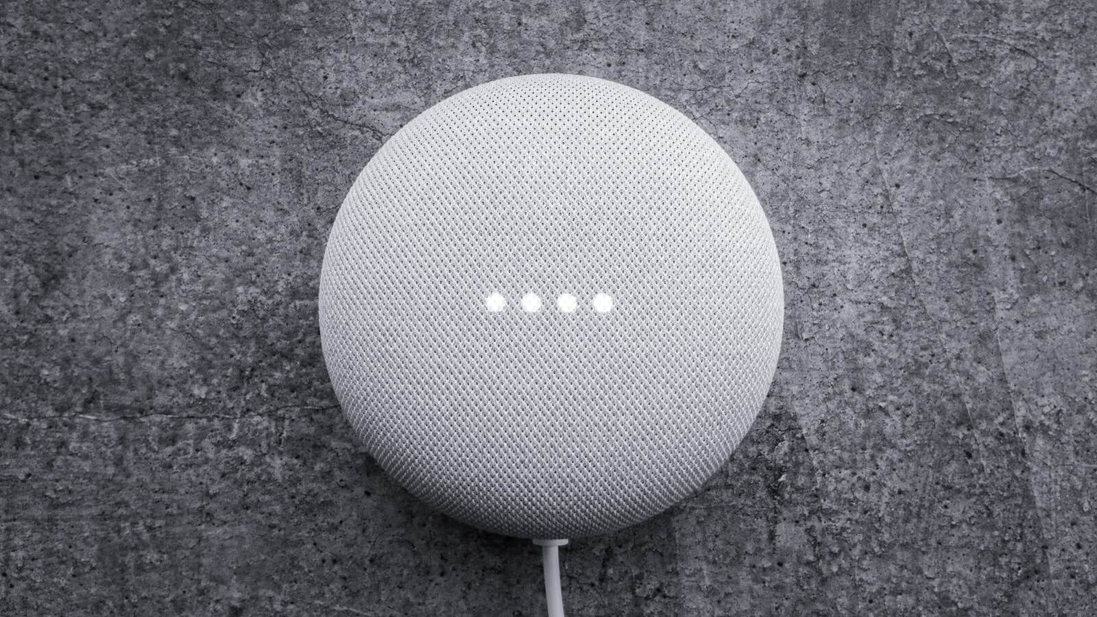 A Google Nest Mini speaker on a slate surface with its four indicator lights lit.
