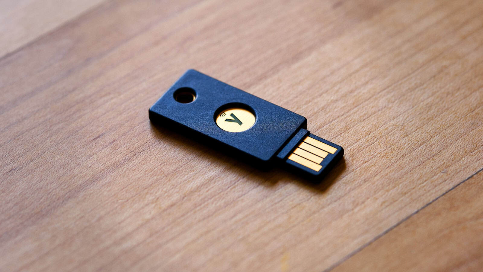 A blue hardware security key with a gold contact plate lying on a wooden desk.