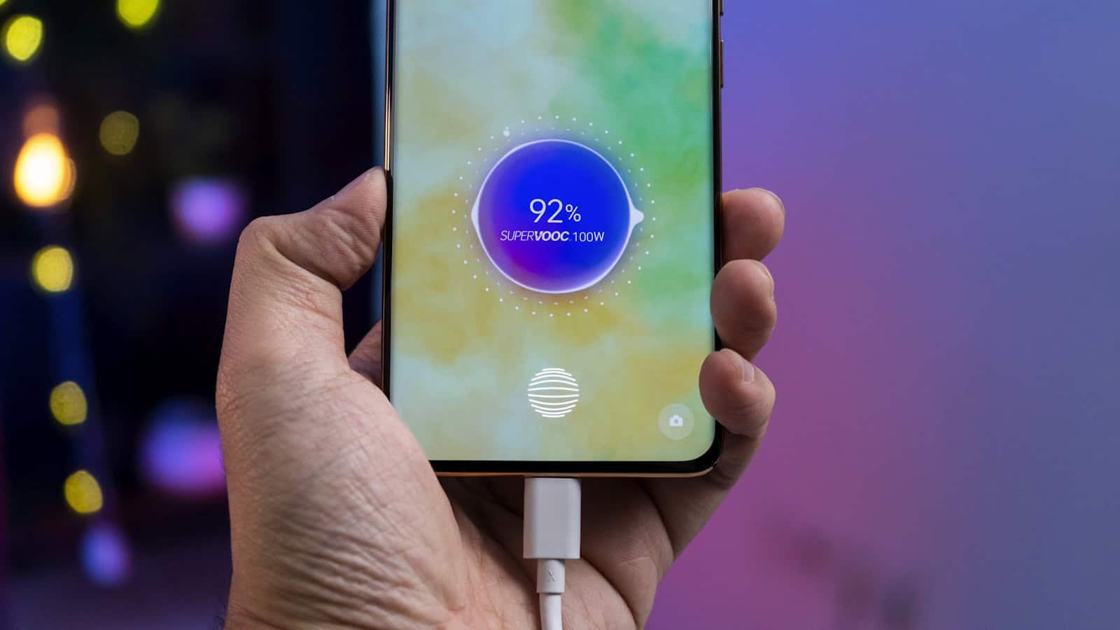 A hand holding an Android phone charging at 92 percent with the cable plugged in.