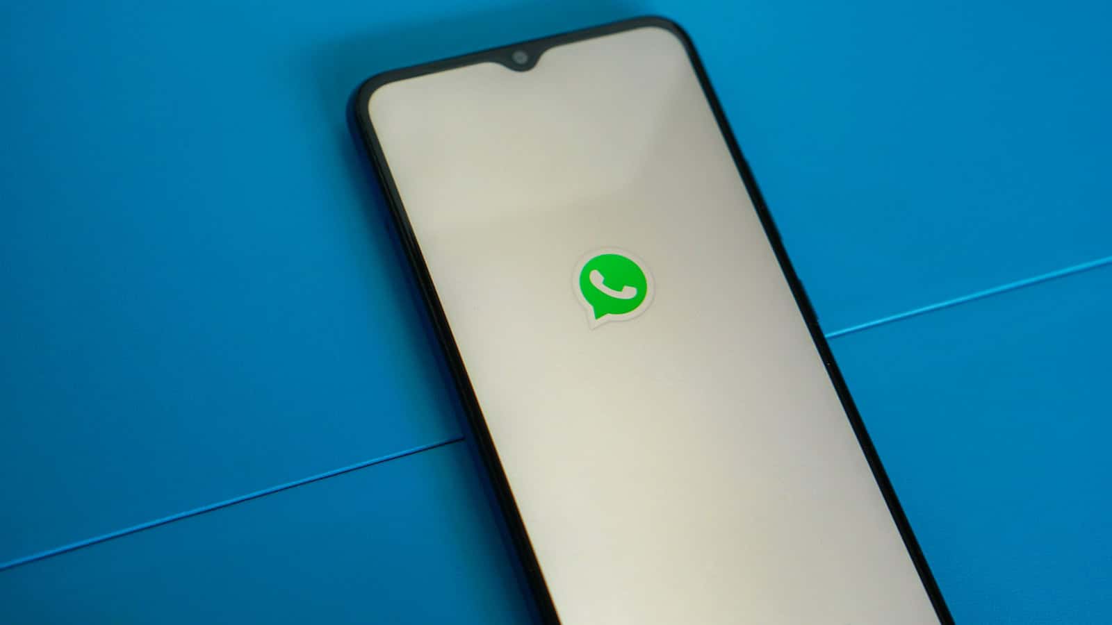 An Android phone on a blue surface showing the WhatsApp logo on its screen.
