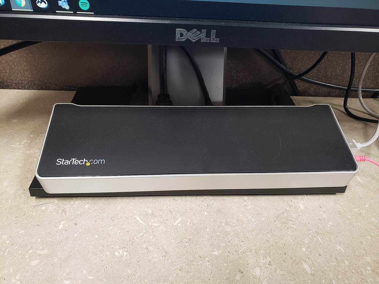 A StarTech USB-C docking station sitting under a Dell monitor with cables attached